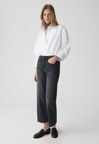 Chemise blanche à manches longues, jean noir taille haute et large, mocassins noirs et une écharpe à motifs autour du cou.