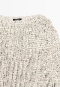 Maglione lavorato a maglia intrecciata color crema e beige con scollo rotondo, maniche lunghe e etichetta Massimo Dutti sul retro del colletto.