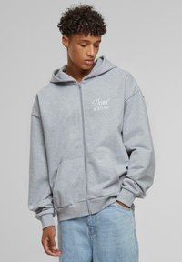 Siva zip-up dukserica napravljena od mekanog materijala, s prednjim dzepom, rebrastim rukavima i natpisom "Dead WRONG" ispisanim bijelom bojom na lijevoj strani prsa.