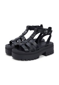 Μαύρα σανδάλια πλατφόρμας με φαρδιές, σταυρωτές λουρίδες. Κατασκευασμένα από απαλό υλικό, με ανάγλυφη σόλα και ρυθμιζόμενα αγκράφες ως διακοσμητικά στοιχεία.