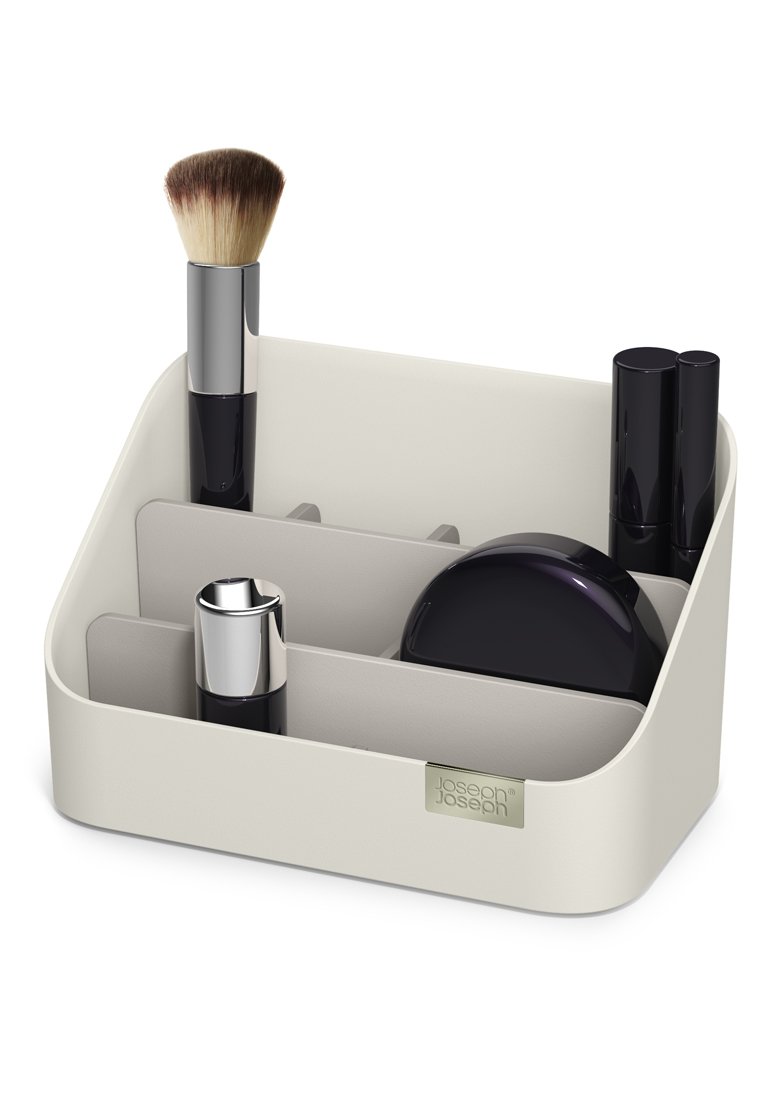 Make-up-Organizer aus hellbeigem Kunststoff mit mehreren Fächern. Enthält einen Make-up-Pinsel, Lippenstifte und einen kompakte Spiegel in dunklen Farben.