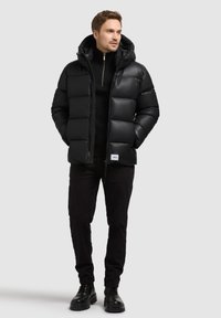 Giacca puffer nera con cappuccio, dotata di chiusura con zip, design trapuntato e texture morbida. Abbinata a pantaloni neri e stivali.