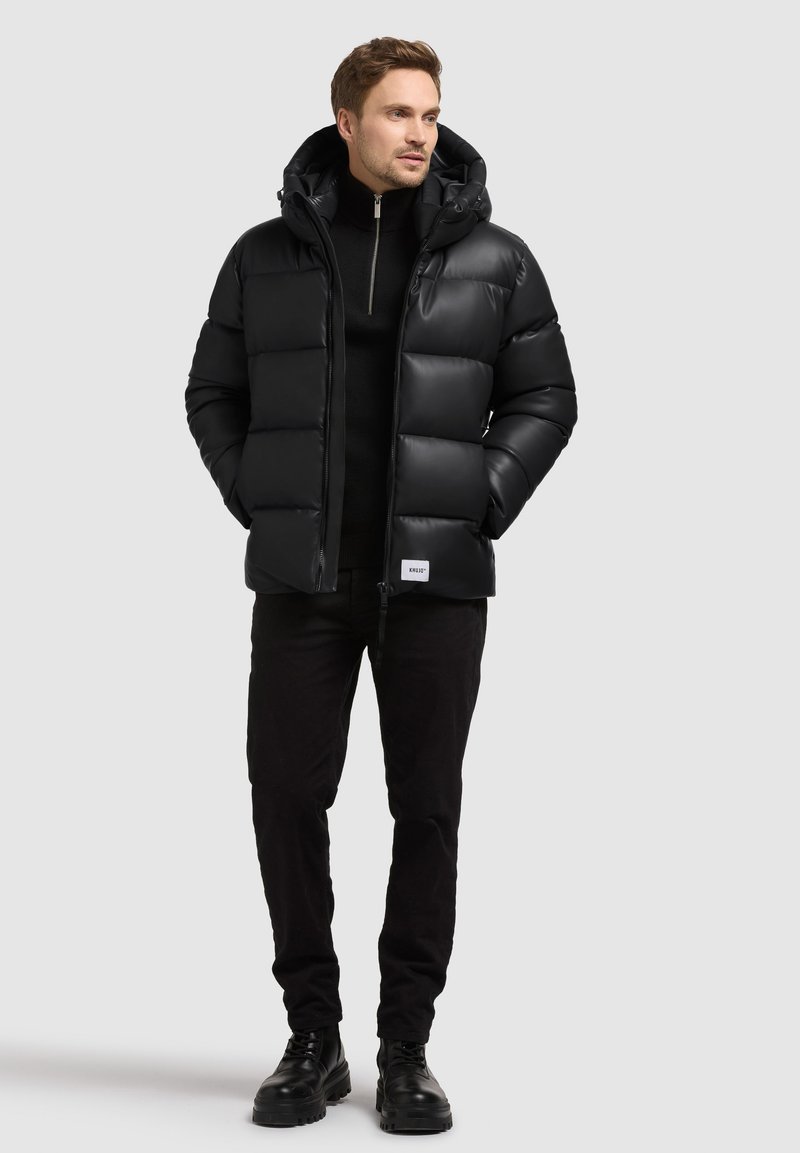 Giacca puffer nera con cappuccio, dotata di chiusura con zip, design trapuntato e texture morbida. Abbinata a pantaloni neri e stivali.