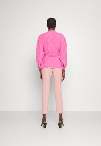 Blusa rosa a fantasia con maniche a sbuffo, stretta in vita, abbinata a pantaloni slim fit rosa chiaro e sandali con tacco.