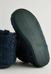 Zapatillas de color azul marino con una parte superior de punto texturizado, forro de tela suave y una suela exterior de goma flexible con un patrón de tracción ondulado. Etiqueta de tamaño visible.