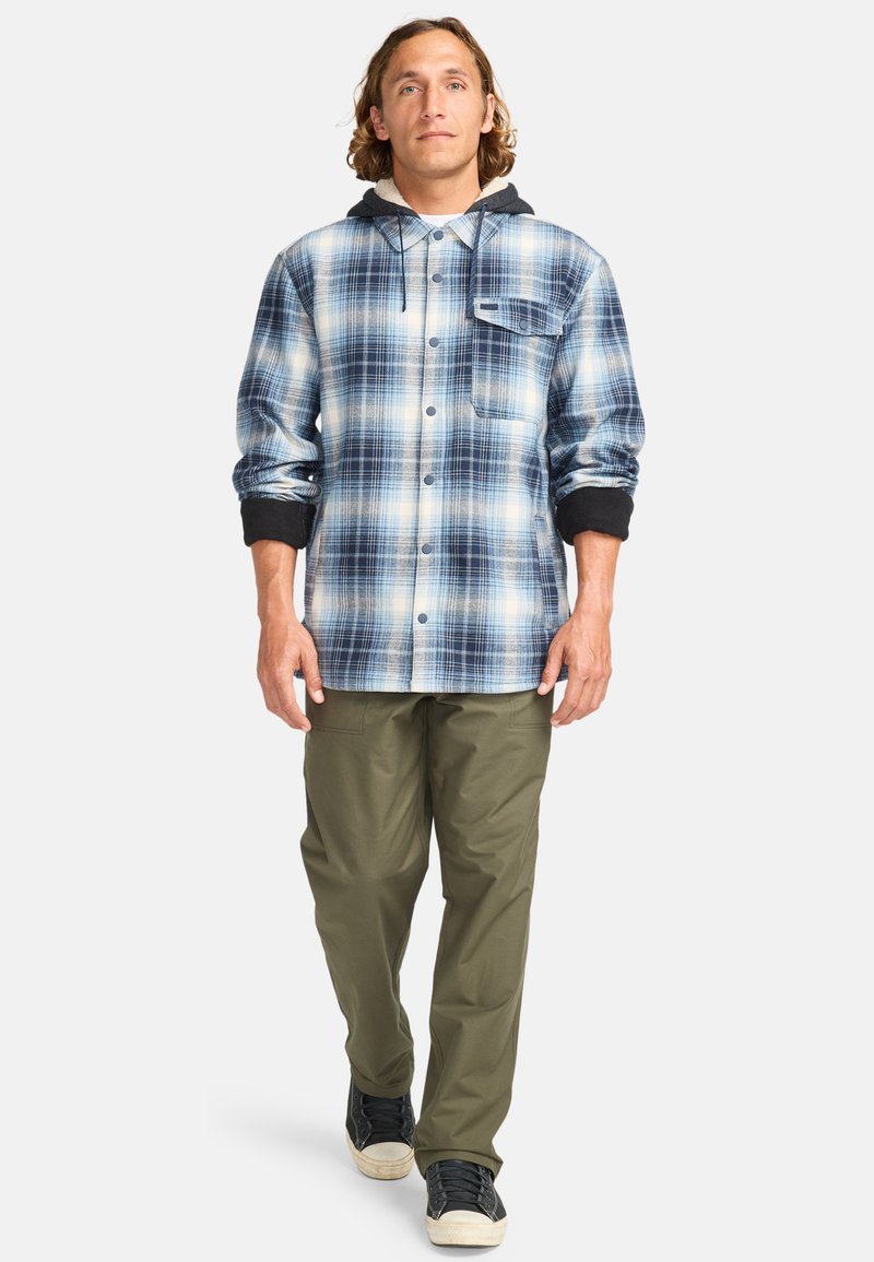 Plaid button-up shirt in blue and white, with black cuffs and hood; paired with olive green pants and black sneakers. Large chest pocket visible.
