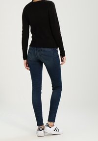 Jeans ajustados de color azul oscuro con una textura suave, combinados con un suéter negro de manga larga y zapatillas blancas con rayas negras.