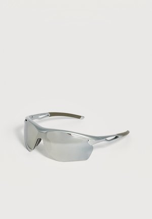 Lunettes de sport à monture argentée avec verres miroirs enveloppants et branches ventilées reposant sur une surface blanche.