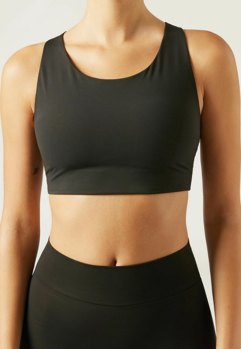 Schwarzer, nahtloser Sport-BH mit Rundhalsausschnitt und breiten Schulterträgern. Glatte Textur, mittellange Crop-Länge, entworfen für Sportbekleidung.