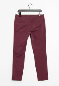 Pantalon stretch bordeaux à coupe slim, avec poches arrière et texture lisse, présenté sur un cintre noir contre un fond blanc.