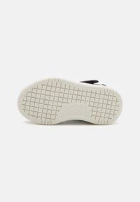 Crne tenisice s fleksibilnom bijelom gumiranom potplatom koja ima teksturirani uzorak za prianjanje. Ime branda "SKECHERS" utisnuto je sa strane.