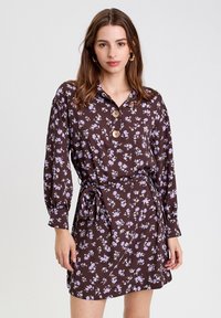 Robe florale marron avec des fleurs violettes, manches longues, col avec boutons, taille cintrée et un tissu léger pour un ajustement décontracté.