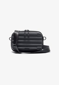 Kompakt sort taske med rillet overflade, justerbar rem, dobbelt lynlås og cirkulært logo accent. Fremstillet af holdbart materiale.