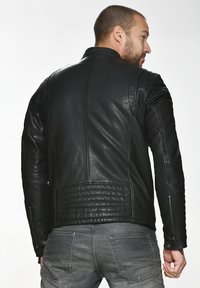Schwarze Lederjacke mit tailliertem Design, gesteppter Rückenpartie und seitlichen Reißverschlusstaschen. Glatte Textur und minimalistischer Stil.