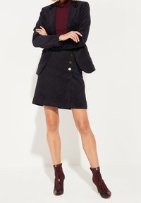 Navy corduroy-puku ja hamekokoelma kultaisilla napilla. Burgundinväriset nilkkurit, joissa on vetoketjusulku ja lakattu nahka.