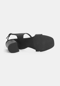 Zwarte hak sandaal met een vierkante neus, verstelbare enkelband en een gestructureerde zool. Gemaakt van glad materiaal met een matte afwerking.