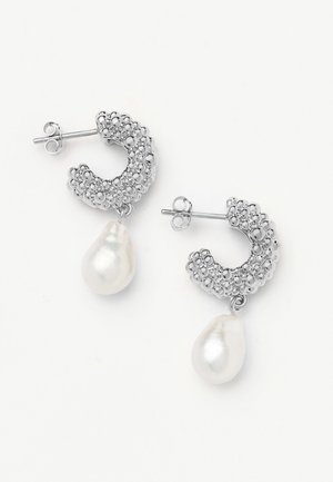 Srebrne kolczyki-koła o teksturowanej powierzchni z nieregularnymi białymi perłami w kształcie kropli, z zapięciami na sztyft, na białym tle.