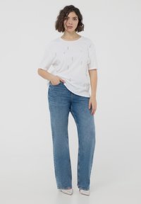 T-shirt bianco a maniche corte con piccoli elementi decorativi argentati, abbinato a jeans a gamba larga blu chiaro e scarpe con tacco alto argentate.