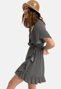 Black and white checkered wrap dress with short sleeves, ruffled hem, and tie belt; made from lightweight fabric for a relaxed fit.