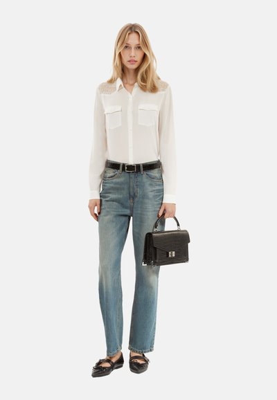 Blusa bianca con maniche lunghe e dettagli in pizzo, due tasche sul petto; jeans blu chiaro a gamba dritta; borsa nera in pelle goffrata coccodrillo; ballerine nere.