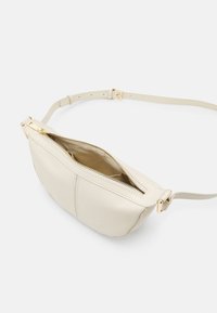 Borsa a tracolla in pelle beige con texture liscia, chiusura a zip e tracolla regolabile. Presenta accessori in oro e dettagli cuciti.