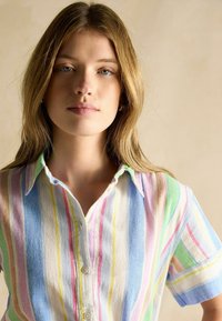 Kurzarmhemd mit Knopfleiste und senkrechten Streifen in Pastellfarben, aus leichtem Stoff mit weicher Textur und Kragen.