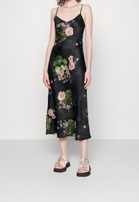 Svart blommig klänning i sidentyg med rosa blommor och gröna löv; har tunna axelband och når mitt på vadbenet.