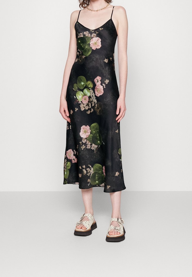 Svart blommig klänning i sidentyg med rosa blommor och gröna löv; har tunna axelband och når mitt på vadbenet.