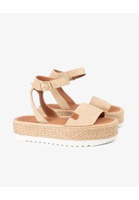 Sandalias de plataforma de ante beige con una suela intermedia de yute trenzado, correa ajustable en el tobillo y diseño de punta abierta que presenta una insignia de cuero.