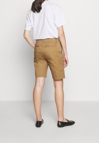 Szorty khaki z tylnymi kieszeniami, prostym przodem i mankietowanym dołem, w połączeniu z białym t-shirtem i czarnymi mokasynami.