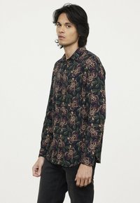 Langsleeve overhemd met een donkergroene achtergrond en bloemenprint in paars en beige. Zachte stof, standaard kraag en een relaxte pasvorm.