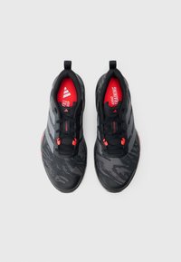 Μαύρα αθλητικά παπούτσια με υφή στην επιφάνεια, με κόκκινες λεπτομέρειες, τρεις γκρι ρίγες και μαλακό πάτο με την ένδειξη "ADIDAS TRAINING".