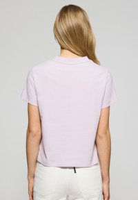 Licht paarse katoenen t-shirt met korte mouwen, ronde halslijn en een cropped ontwerp. Effen textuur, geen patronen of versieringen.