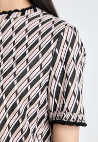 Knit short-sleeve top featuring a diagonal plaid pattern in pink, beige, and black. Scalloped neckline and hem. Soft texture.