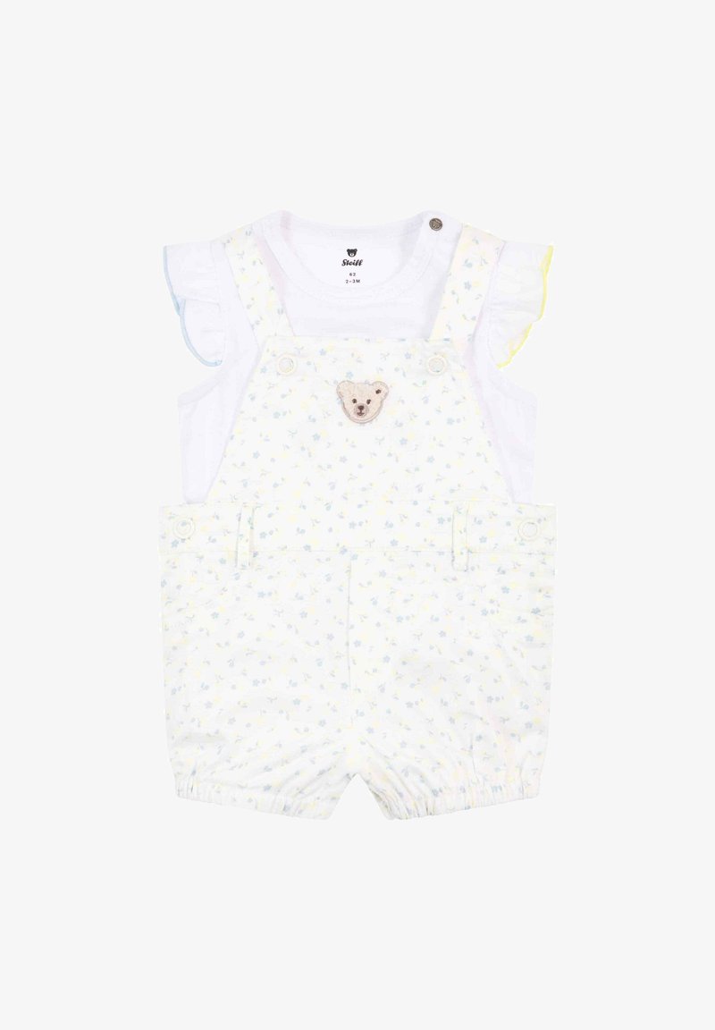 Shortalls blancs avec un motif floral bleu clair et jaune, présentant une appliqué d'ours, des boutons-pression aux épaules et des manches blanches froncées.