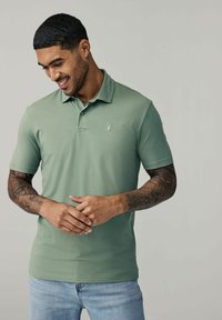Polo de manga corta para hombre en verde claro, hecho de mezcla de algodón. Presenta un collar, una abertura con tres botones y un pequeño logo en el pecho.