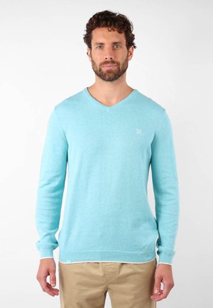 Pull en v bleu clair en matériau doux, avec des manches longues, un ourlet côtelé et un petit logo sur la poitrine.