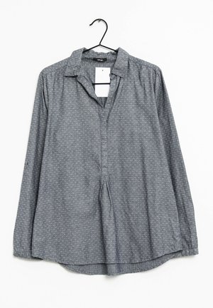 Grå langærmet skjorte med krave, der har et subtilt textured mønster og en delvis knaplukning, hængt på en sort krog.