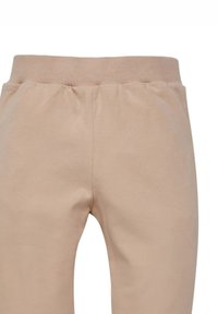 Pantaloni della felpa di un beige chiaro con una cintura elastica a coste e materiale in cotone morbido. Presentano un design semplice e una texture liscia.