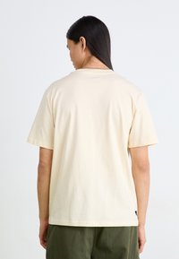 Krämfärgad bomulls-t-shirt med korta ärmar och en avslappnad passform. Har en rund halsringning och inga synliga logotyper eller mönster.