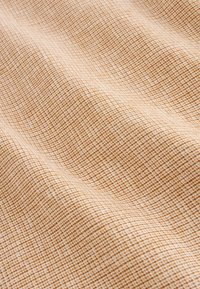 Tissu beige et blanc avec un petit motif à carreaux, présenté avec des plis doux et une texture agréable.