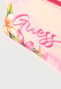 Ροζ υφασμάτινη θήκη με κεντητό λογότυπο «Guess» και τροπικό λουλουδάτο σχέδιο που περιλαμβάνει πορτοκαλί και ροζ άνθη με πράσινα φύλλα.