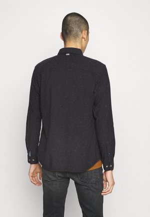 Chemise à manches longues bleu foncé avec une texture mouchetée, dotée d'un col, de poignets à boutons et d'un ourlet arrondi. La vue arrière montre les coutures des épaules et l'étiquette de logo.