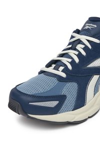 Mėlyni ir tamsiai mėlyni Reebok sportbačiai su baltais raišteliais, tinklelio ir zomšo elementais bei paminkštintu baltu padu, rodomi iš arti iš priekio.