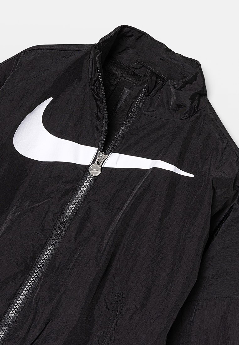 Veste Nike noire avec une fermeture éclair intégrale, un col haut et un grand logo swoosh blanc sur la poitrine. Fabriquée en matériau léger et texturé.