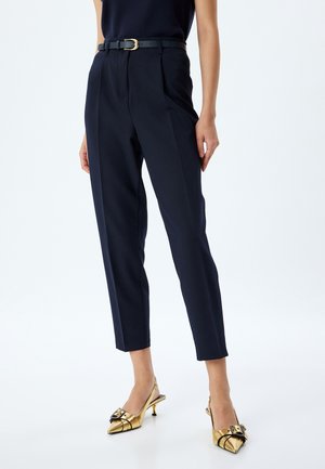 Navy tailored trousers with a high waist, sharp crease, and a black belt featuring a gold buckle; paired with gold slingback heels.