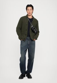 Cardigan ribbed de culoare verde închis, cu nasturi mari, purtat peste o cămașă navy. Asortat cu blugi largi de culoare albastră și pantofi negri. Mică geantă neagră.