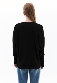 Maglione nero a maniche lunghe con una vestibilità comoda e polsini a costine, abbinato a jeans in denim blu chiaro, visto da dietro su uno sfondo bianco.