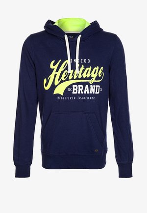 Felpa blu navy con interno verde neon a contrasto, dotata di tasca anteriore e grafica stampata. Indossata con jeans azzurri e scarpe da ginnastica nere.