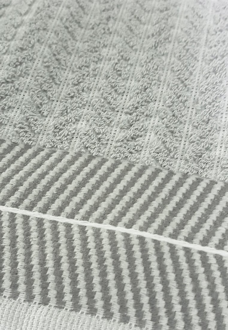 Textil mit einem hellgrauen und weißen Streifenmuster, das eine erhöhte Textur und gerippte Details aufweist, wobei der taktile Kontrast und das Design betont werden.